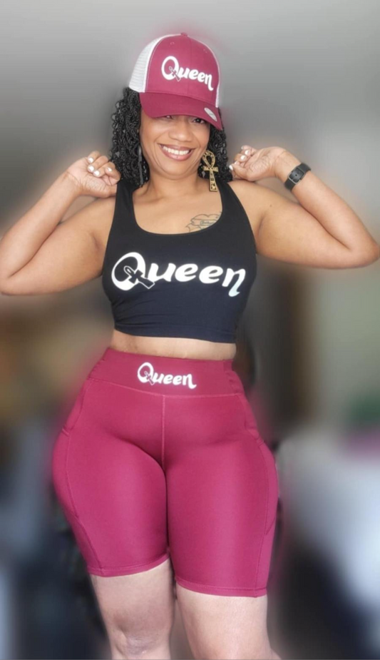black crop top and maroon shorts with 'Queen' printed on them, standing against a blurred background.
